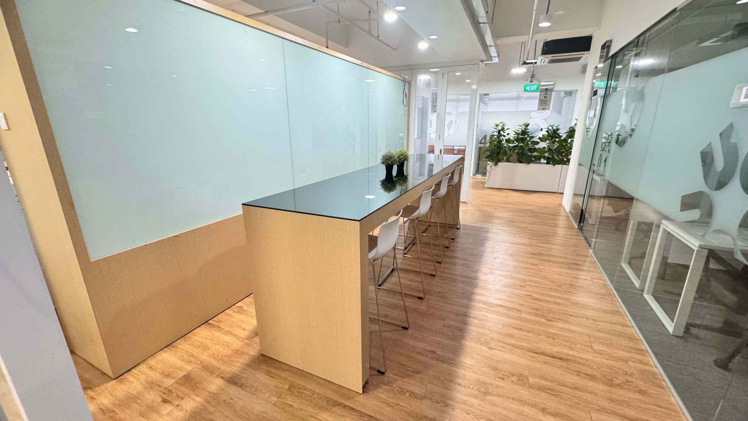 A well-lit coworking space featuring a long, sleek communal table with a glossy black surface, paired with modern white bar stools.