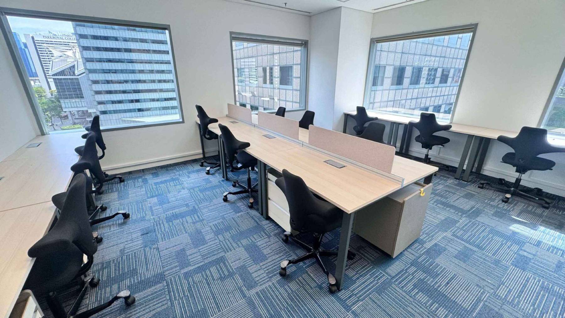A bright and spacious coworking area featuring rows of desks with ergonomic black chairs, designed for maximum productivity.